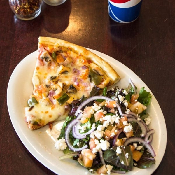 A slice of Pizza On Tap pizza with bell peppers and onions, served with a side salad.