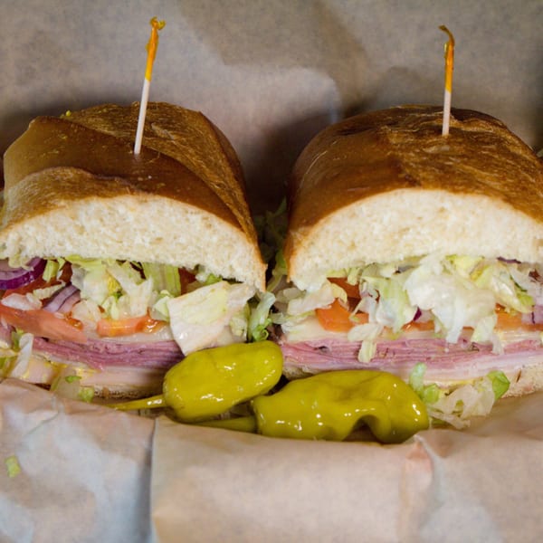 A large deli sub sandwich, cut in half, with meats, cheese, lettuce, tomato, and onion.
