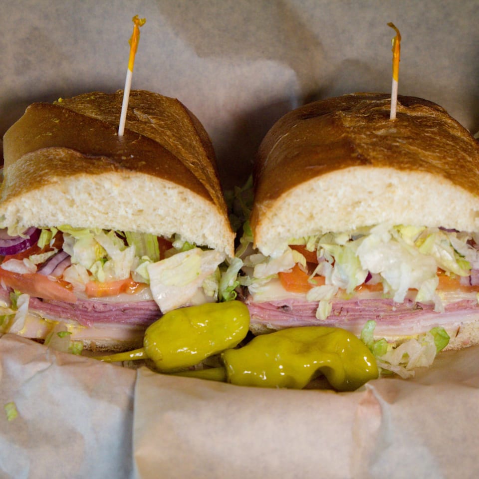 A large deli sub sandwich, cut in half, with meats, cheese, lettuce, tomato, and onion.