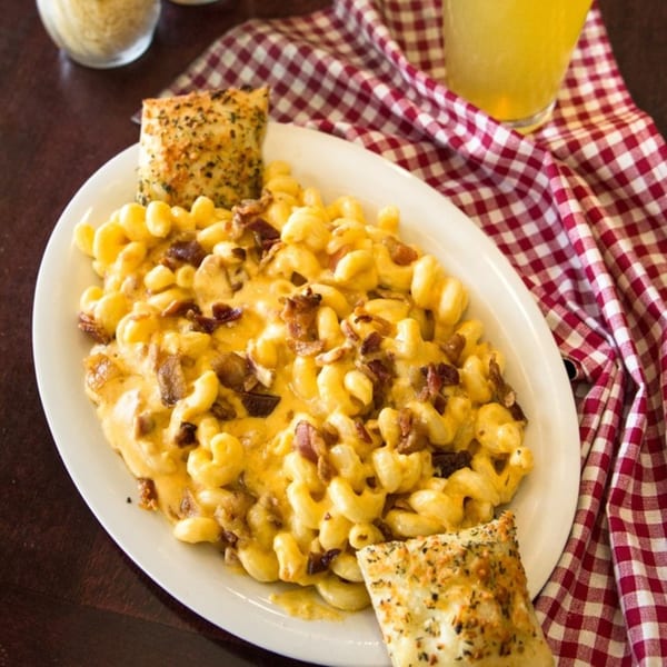 Creamy mac and cheese with bacon bits and two pieces of garlic bread on a white plate.