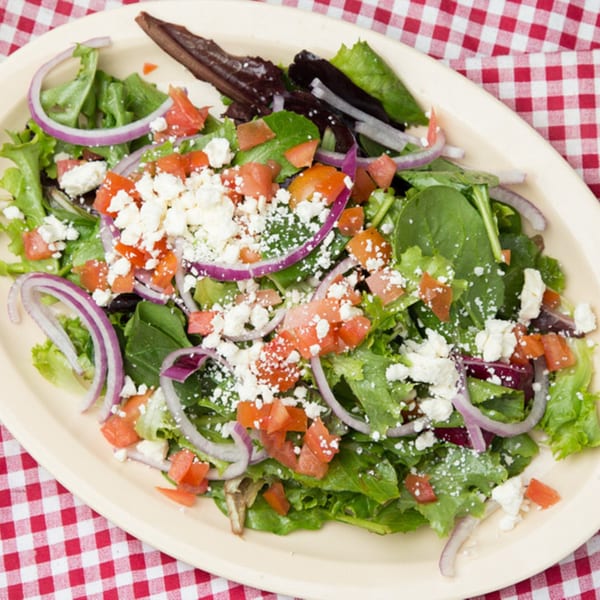 A fresh salad with mixed greens, red onions, diced tomatoes, and crumbled feta cheese.