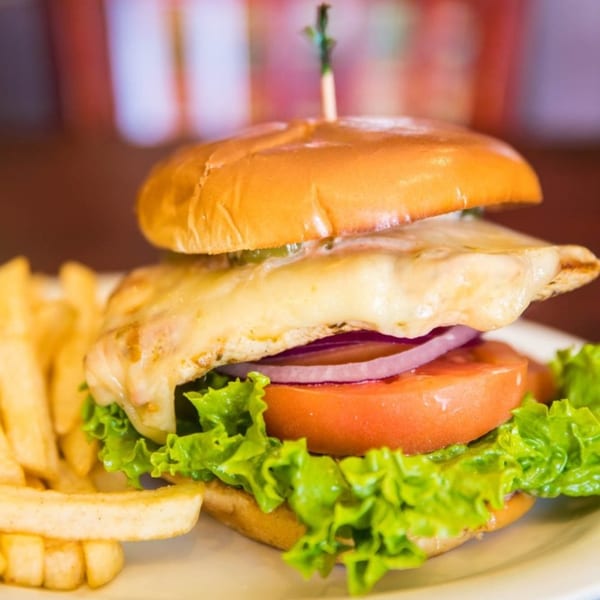 Chicken sandwich with melted cheese, lettuce, tomato, and onion, served with fries.